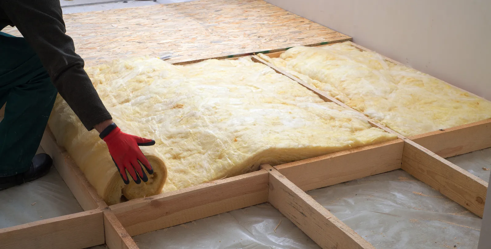 Loft insulation rolling out mineral wool over joists